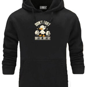 Könnte beinhalten: Schwarzer Kapuzenpullover mit Frontaufdruck. Der Aufdruck zeigt eine Cartoon-Ente, die Gewichte hebt, mit dem Text "DON'T FART" darüber und "DON'T FART, DON'T FART" darunter. Der Pullover hat eine Vordertasche.