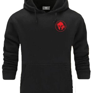 Peut inclure: Sweat-shirt à capuche noir avec un graphique de casque de spartiate rouge sur la poitrine gauche. Le graphique est à l'intérieur d'un cercle avec un effet de projection rouge.