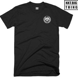 May include: Black t-shirt with a white graphic of an eagle with a wreath around it and the text "NXTBIGTHING" underneath.