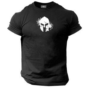 Puede incluir: Camiseta negra con un gráfico blanco de un casco espartano con un salpicón de pintura blanca detrás.