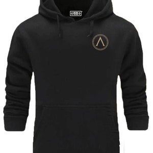 Peut inclure: Sweat-shirt à capuche noir avec un logo brodé or sur la poitrine gauche. Le logo est un cercle avec une lettre A stylisée à l'intérieur. Le texte "MYSTIC FITNESS" est imprimé sur une petite étiquette sur le sweat-shirt.
