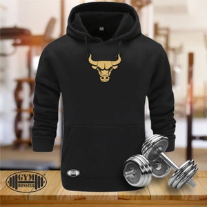 Op de afbeelding: Zwart hoodie met een gouden stierenlogo op de voorkant. De hoodie heeft een kangoeroezak en een capuchon met trekkoord. De tekst "GYM MONSTER" is afgedrukt op de linkerbenedenhoek van de hoodie.