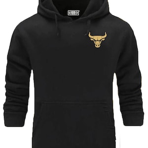 Peut inclure: Sweat-shirt à capuche noir avec un logo de taureau doré sur le devant. Le logo est une tête de taureau stylisée avec des cornes.