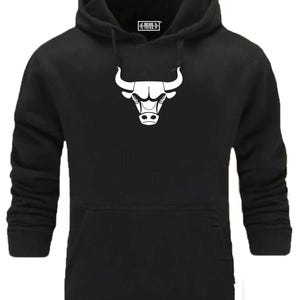 Könnte beinhalten: Schwarzer Kapuzenpullover mit einem weißen Bullenlogo auf der Vorderseite. Das Logo ist ein stilisierter Bullenkopf mit Hörnern.