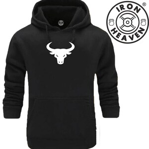 Op de afbeelding: Zwarte hoodie met een wit stierenkoplogo en de tekst "IRON HEAVEN" in een cirkel met een gewichtsymbool aan beide kanten.