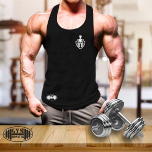 Könnte beinhalten: Ein schwarzes ärmelloses Tanktop mit einer weißen Grafik eines spartanischen Helms in einem Schild. Der Text "GYM MONSTER" ist in Weiß auf einem schwarzen Oval am unteren Rand des Shirts gedruckt.