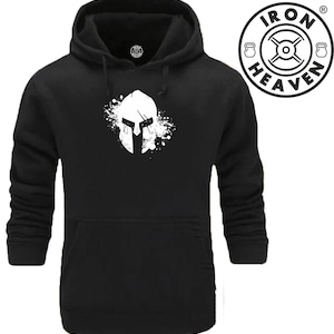 Peut inclure: Sweat-shirt à capuche noir avec un graphique blanc d'un casque de spartiate avec une éclaboussure de peinture derrière. Le texte "IRON HEAVEN" est dans un cercle avec un poids de chaque côté.