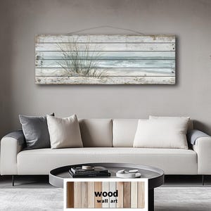 Peut inclure: Tableau mural en bois représentant une scène côtière avec une vue sur la plage et l'océan. L'œuvre est montée sur un fond de planches de bois clair vieilli. L'image comprend un canapé, des coussins et une table basse.