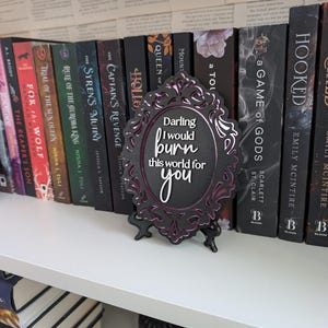 May include: A black framed decorative sign with a purple and black design. The sign has the text "Darling I would burn this world for you" in white lettering.