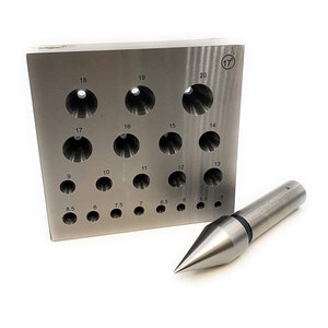 Op de afbeelding: Een set metalen ponsen in verschillende maten, variërend van 5 tot 20 mm. De set bevat een ponshouder met een raster van gaten en een puntig ponsgereedschap.