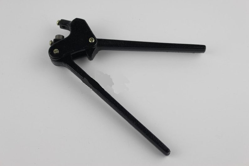 Puede incluir: Una herramienta de perforaci&oacute;n manual de metal negro con dos mangos largos, un punto de pivote asegurado con un tornillo met&aacute;lico y un peque&ntilde;o mecanismo de cabezal perforador en la parte superior para hacer agujeros mediante presi&oacute;n manual.