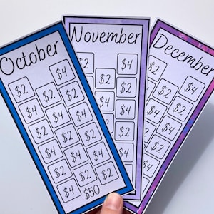 May include: Three colorful savings tracker cards for October, November, and December. Each card has a different border color and features boxes with dollar amounts. The cards are designed to help track savings goals.