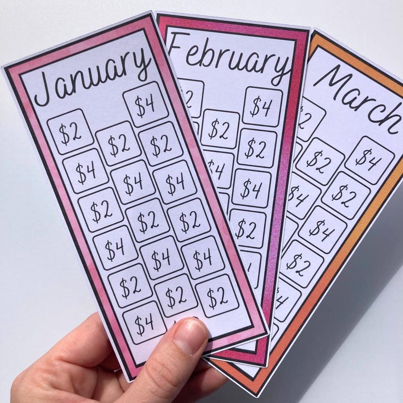 May include: Three colorful savings tracker cards for January, February, and March. Each card has a different colored border and features a grid of boxes with dollar amounts. The cards are held in a hand.