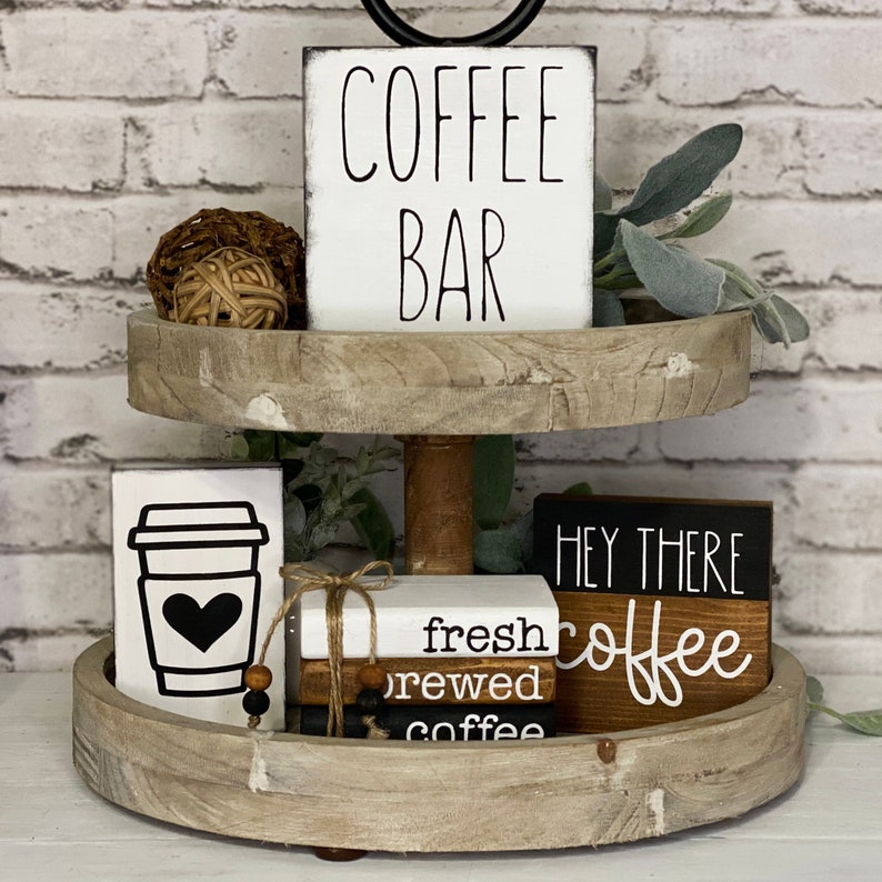 Może przedstawiać: Dwupoziomowa drewniana taca z r&oacute;żnymi drewnianymi tabliczkami z motywem kawy. G&oacute;rny poziom ma białą tabliczkę z napisem "COFFEE BAR". Dolny poziom ma białą tabliczkę z czarnym kubkiem kawy i sercem, białą tabliczkę z tekstem "fresh brewed coffee", czarną tabliczkę z napisem "HEY THERE" i brązową tabliczkę z napisem "coffee".