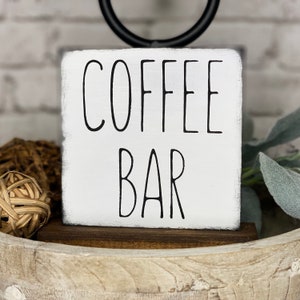 Może przedstawiać: Biały drewniany znak z czarnym napisem "COFFEE BAR". Znak stoi na drewnianej podstawie.