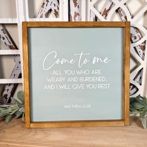 May include: Square wooden framed sign with a light blue background and white script that reads "Come to me, all you who are weary and burdened, and I will give you rest." The text "Matthew 11:28" is at the bottom.