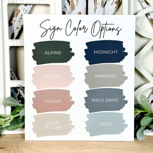 May include: A white sign with the text "Sign Color Options" in script. Below, nine paint swatches display colour choices including Alpine, Midnight, Blush, Mineral, Mauve, Maui Sand, Sand Dollar, and Sage. The sign is set against a rustic, white-washed wooden background.