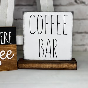 Może przedstawiać: Biały drewniany znak z czarnym napisem "COFFEE BAR" na brązowym drewnianym stojaku.