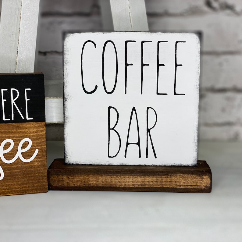 Może przedstawiać: Biały drewniany znak z czarnym napisem "COFFEE BAR" na brązowym drewnianym stojaku.