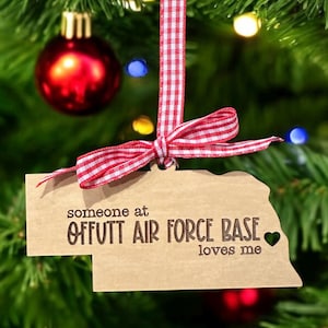 May include: A wooden Christmas ornament shaped like the state of Nebraska with the text "someone at Offutt Air Force Base loves me" and a small heart.