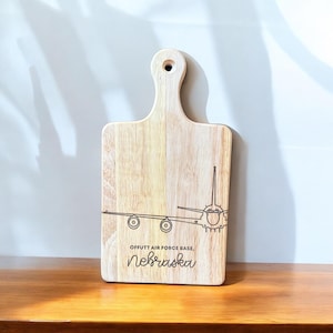 May include: A wooden cutting board with a laser-etched design of an airplane and the text "Offutt Air Force Base, Nebraska".