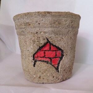 May include: A small, gray concrete planter with a red brick design painted on the side.
