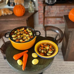 May include: Miniature kitchen scene featuring a small orange pot and bowl filled with stew, alongside carrots and potatoes. A pumpkin and miniature furniture complete the cozy, autumnal setting.