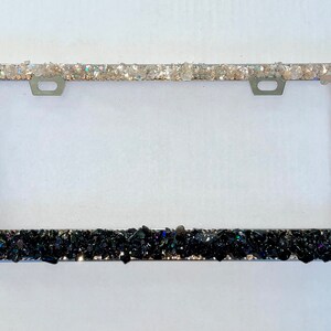 May include: A silver license plate frame with a black and white glitter design. The top half of the frame is covered in white glitter, while the bottom half is covered in black glitter.