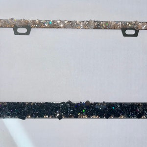 May include: A silver license plate frame with a black and white glitter border. The top border is white glitter and the bottom border is black glitter.