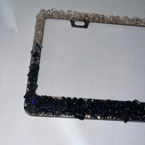 May include: A black and clear crystal embellished license plate frame. The frame is made of metal and has a black finish. The crystals are arranged in a random pattern around the frame.