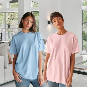 May include: Two short-sleeved t-shirts, one light blue and one pink. Both shirts have a crew neck and a relaxed fit. The models are standing in front of a window with natural light.