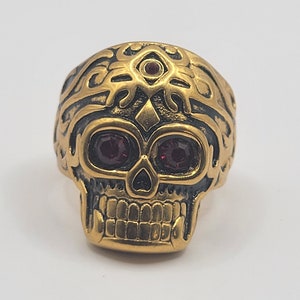May include: Gold skull ring with ruby red eyes and intricate details.