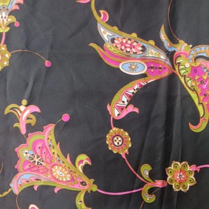 Op de afbeelding: Donkergrijze stof met een herhalend paisley-patroon in roze, groen, blauw en wit. Het ontwerp bevat gestileerde bloemen- en bladmotieven met gebogen lijnen en ingewikkelde details, waardoor een levendig en sierlijk textiel ontstaat.