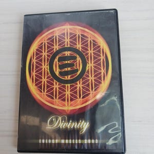 May include: A DVD case with a black background featuring a circular design in shades of orange and yellow. The design has a central symbol and intricate patterns. The word "Divinity" is written in cursive, with "EULOGY WHEELS 2003" below.