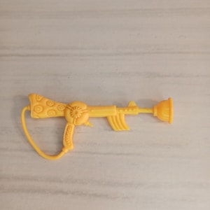 May include: A yellow toy gun with a plunger at the end. The toy gun has a floral design on the stock and a trigger. The gun is made of plastic and is a bright yellow color.