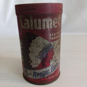 Puede incluir: Lata de polvo para hornear Calumet Double-Acting vintage. La lata roja y plateada presenta un perfil nativo americano y las palabras "Recipe Book". La lata cilíndrica muestra signos de desgaste, con un peso neto de 198g.