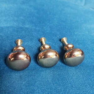 May include: Three round cabinet knobs with a polished metallic copper finish. Each knob features a smooth, spherical head attached to a short, cylindrical mounting post with a threaded screw base, designed for attachment to furniture or cabinetry.