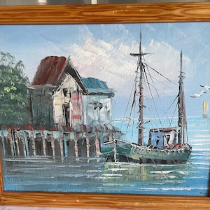 Op de afbeelding: Een schilderij van een klein vissersbootje dat aangemeerd ligt aan een houten pier. Het bootje is groen en blauw met witte zeilen. De pier is gemaakt van verweerd hout en er staat een klein gebouwtje achter. Het schilderij is in een realistische stijl geschilderd met de nadruk op de details van het bootje en de pier.