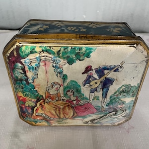 May include: A vintage tin box with a colorful illustration of a man playing a lute for two women in a garden setting. The text "The Music Lesson" is visible on the bottom of the box.