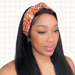 May include: A woman with long black hair is wearing a knotted headband with a floral pattern in shades of orange, red, and white.