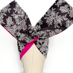 May include: A black and white floral print headband with a bright pink trim. The headband is tied in a knot at the top, creating a stylish accessory. The floral pattern is a delicate design.
