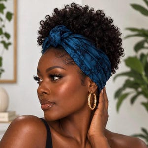 May include: A dark blue knotted headband with a subtle black marbled pattern worn over dark curly hair. The accessory features a central twist detail at the front and is paired with large gold hoop earrings that hang from the earlobes.