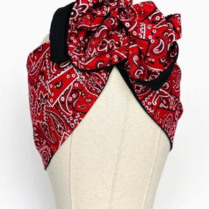 May include: Red bandana headband with a large bow, featuring a paisley pattern. The headband is trimmed with black fabric.