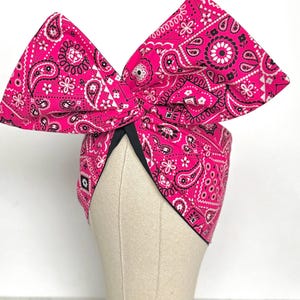 Op de afbeelding: Een roze bandana met een zwart paisley-patroon gebonden in een strik op een mannequinhoofd.
