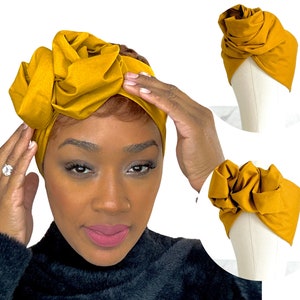 Peut inclure: Turban jaune moutarde avec un grand ornement en tissu en forme de rose. Le couvre-chef est présenté sur une personne et deux mannequins. Le tissu semble doux et le turban est probablement conçu pour la mode ou la protection des cheveux.