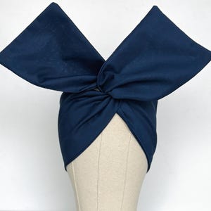 May include: A navy blue fabric headband with a large bow on top. The headband is tied in a knot at the back of the head.