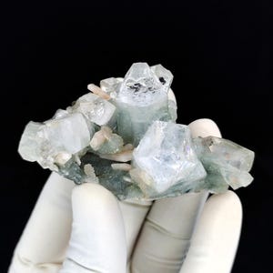 May include: A mineral specimen featuring translucent, pale green, hexagonal crystal formations clustered together. The cluster includes several sharp, clear points and smaller, opaque white crystalline structures embedded within a dark green base matrix.