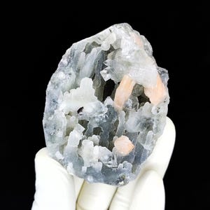 May include: A raw mineral specimen featuring a cluster of translucent white and pale peach-colored crystalline structures. The formation has a jagged, irregular shape with a textured surface, showcasing a mix of clear, frosty, and soft orange hues.