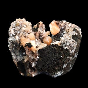 May include: A close-up of a mineral specimen featuring a dark, porous base with clusters of peach-colored crystals and smaller, clear crystals. The mineral formation is set against a black background.