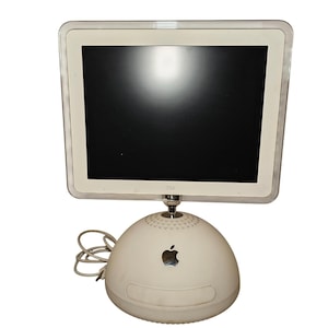 Può includere: Un computer desktop Apple iMac G4 bianco con schermo piatto e cornice bianca, montato su un braccio cromato regolabile fissato a una base emisferica bianca con un logo Apple argentato e un cavo di alimentazione che sporge dal lato.